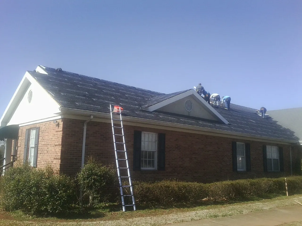 Crew tearing shingles off a brick ranch roof with a ladder set — Metal Roof Repair work by our crew in Gilbert